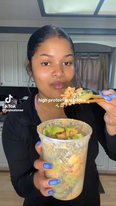 a woman eating food from a plastic cup with chopsticks in her hand and looking at the camera