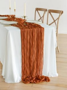 the table is set with two candles and an orange scarf