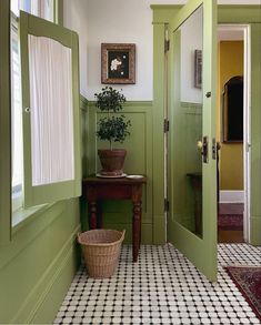 a hallway with green walls and black and white tile flooring next to a potted plant