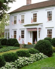 a large white house with american flags on the windows and bushes in front of it