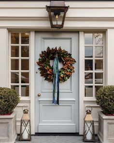 a wreath on the front door of a white house with two planters next to it