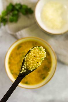 a spoon with some food on it and two bowls in the background, one is filled with broccoli