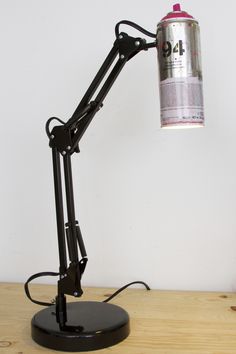 a desk lamp on top of a wooden table next to a wall with a can