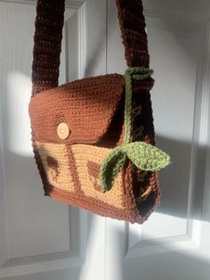 a crocheted purse hanging from a hook on a white door with a green leaf