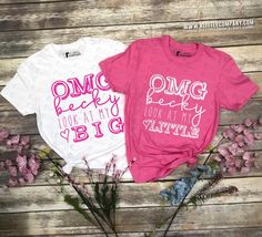 two pink and white shirts sitting on top of a wooden table next to purple flowers