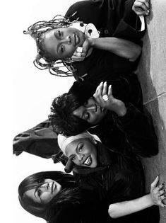 four women leaning against a wall with their arms around each other