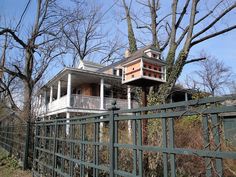 a house with a balcony on top of it next to a green fence and trees