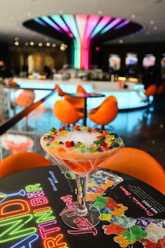 an orange chair with a drink in it on the table at a restaurant that is decorated with neon lights