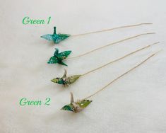 four green origami birds hanging from gold chains on a white background with the words green 1, green 2