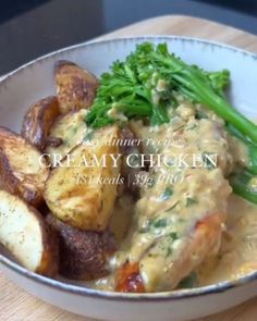 a white bowl filled with potatoes and broccoli covered in gravy on top of a wooden table