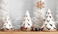 three white ceramic christmas trees sitting on top of a wooden shelf next to some branches