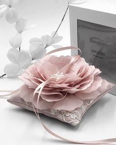 a pink flower sitting on top of a white pillow next to a box and ribbon