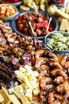 an assortment of food is displayed on a wooden platter with skewers and dips