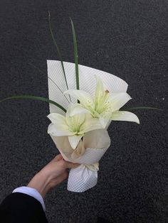 a person holding a bouquet of white flowers in their hand on the ground with asphalt