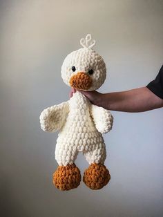 a crocheted white duck with brown feet is held by a person's hand