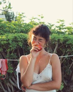 a woman standing in front of a bush eating an apple while wearing a bra top