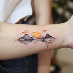 a woman's arm with mountains and an orange sun tattoo on the left forearm