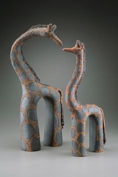 two ceramic giraffes standing next to each other in front of a gray background