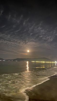 the moon shines brightly in the night sky over the ocean and beach as waves roll on the shore