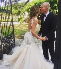 an older man and woman are kissing in front of a wrought iron gate at their wedding