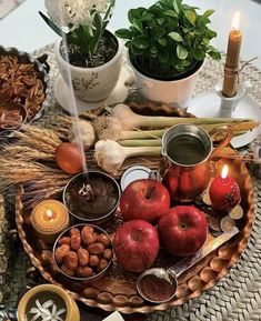 an assortment of food on a table with candles and flowers in the background, including apples