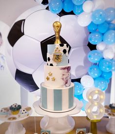 a soccer themed cake sits on a table with blue and white balloons in the background