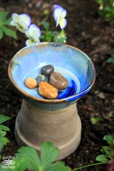 a blue bowl with rocks in it sitting on the ground next to some purple flowers