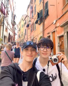 two young men taking a selfie in front of an alleyway with other people