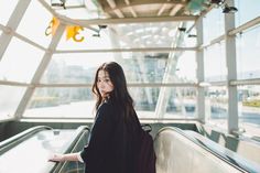 a woman is standing on an escalator with her back to the camera and looking at the camera