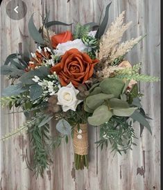 an arrangement of flowers and greenery is displayed on a wooden wall with wood planks