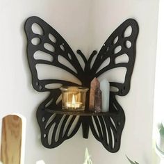 a candle is lit on a shelf with a butterfly shaped wall hanging above it in a bathroom