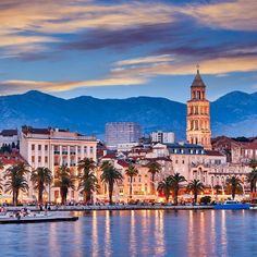 the city is lit up at night with mountains in the background and water reflecting it's lights