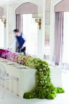 a long table with chairs and flowers on it in front of a man walking by