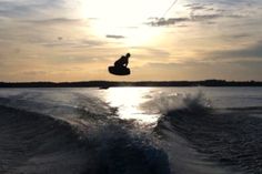 a person on a surfboard in the air above the water at sunset or dawn