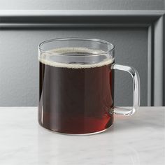 a glass mug filled with liquid sitting on top of a white counter next to a gray wall