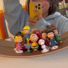 a woman taking a photo of her cell phone with peanuts and friends figurines