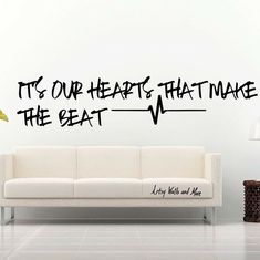 a white couch sitting in front of a wall that says it's our hearts that make the beat