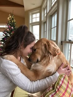 a woman hugging her dog in front of a window with christmas decorations on the windowsill