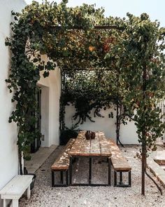 a wooden table sitting under a pergoline covered arbor in front of a white building