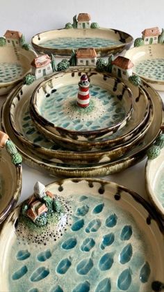 there are many plates on the table with small houses in them and one has a lighthouse