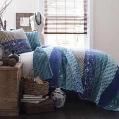 a bed room with a neatly made bed next to a window covered in blue quilts