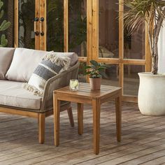 a couch and table on a wooden deck with potted plants in the background,