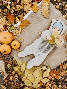 a baby doll laying on top of a blanket surrounded by leaves and pumpkins