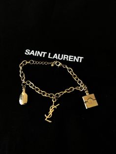 Yves Saint Laurent vintage bracelet around 1970 adorned with pendants imitating perfume bottles and the YSL logo - golden metal - excellent condition despite slight wear in the gilding that you can see on the photos - size in photo - ideal for a gift or for a fashion lover https://antiquairesdesmodes.com Bracelet vintage Yves Saint Laurent vers 1970 orné de pampilles imitant les flacons de parfum et le logo YSL - métal doré - excellent état malgré légère usure de la dorure que vous pouvez voir s Vintage Jewelry With Gold-tone Logo Plaque, Vintage Gold-tone Jewelry With Logo Charm, Gold-tone Metal Jewelry With Logo Plaque, Gold-tone Bracelet With Logo Charm As Gift, Luxury Metal Jewelry With Logo Charm, Metal Bracelet With Logo Charm, Vintage Gold Bracelet With Logo Charm, Elegant Metal Charm Bracelet With Logo Charm, Designer Gold-tone Metal Jewelry