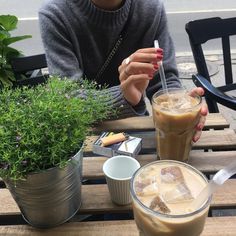 a woman sitting at a table with two drinks in front of her and another drink next to her