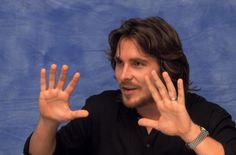 a man with his hands in the air and one hand out to say something while sitting at a table