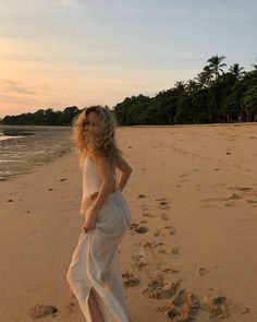 a woman is walking on the beach with her hand in her pocket and footprints behind her