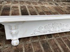 an old white bench sitting on top of a brick floor in front of a wall