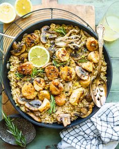 a skillet filled with shrimp and rice on top of a wooden table next to lemon wedges