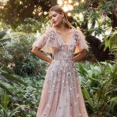 a woman standing in front of some trees wearing a dress with flowers on the side